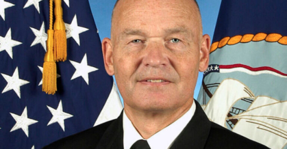 A headshot of former MARAD administrator Mark Buzby, with flags including the U.S. and Navy standard.